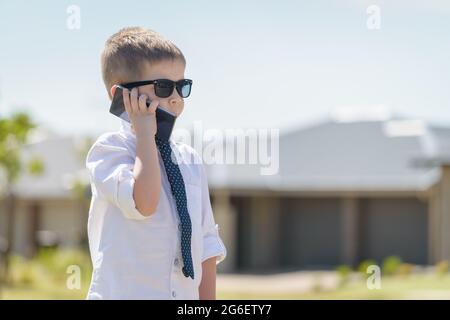 Boy standing and talking on the mobile phone while wearing business attire with sunglasses on a bright summer day Stock Photo