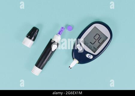 Tools for diabetes treatment with blood glucose sugar meter showing blood sugar of 94 and lancing device with lancet on blue background Stock Photo