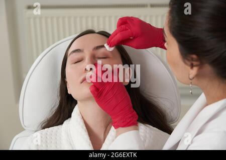 Cosmetologist cleaning face of a patient with cotton pad in beauty and spa salon preparing for procedure Stock Photo