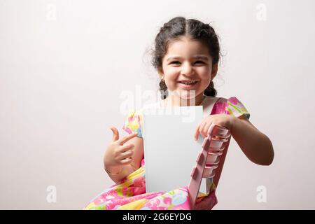 Happy little girl pointing to a story book with blank cover in front of her body, editable mock-up series template ready for your design, book cover s Stock Photo