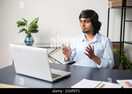 Serious clever indian male office employee making video call, talking ia video connect on the laptop, eastern man in smart casual shirt holding negotiation, discussion aimed at reaching an agreement Stock Photo