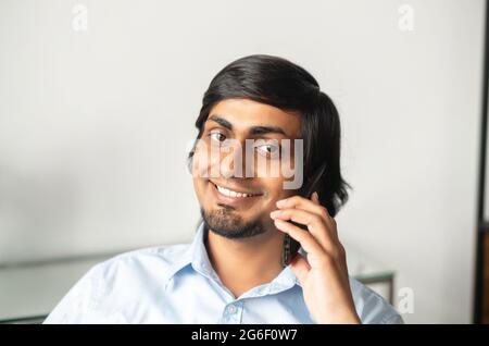 Headshot of smiling indian businessman in smart casual shirt talking on the smartphone and looks at the camera, eastern man has pleasant phone conversation Stock Photo