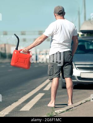 A red canister on the asphalt near the car. The car ran out of gas and stalled. A young man hoping for help on the road from other drivers Stock Photo