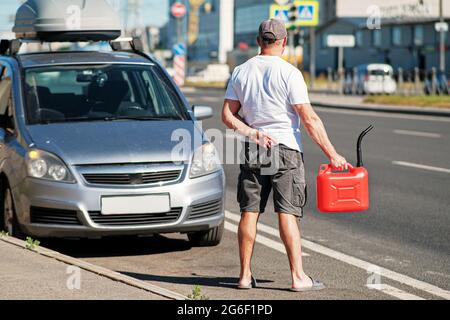 A red canister on the asphalt near the car. The car ran out of gas and stalled. A young man hoping for help on the road from other drivers Stock Photo