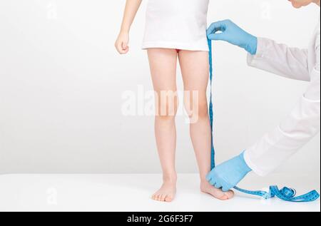 A doctor in blue gloves with a measuring tape measures the length of the legs of a 4-year-old girl. Child development and growth concept Stock Photo