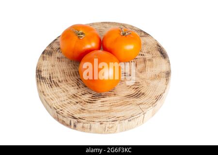 Three orange tomatoes lie on a wooden stand. White background, isolate. Natural fresh yellow tomatoes, close-up, vegetables Stock Photo