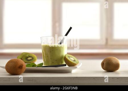 Fruit breakfast with glass of kiwi drink on plate and container cut fruit around on table and window background. Front view. Stock Photo