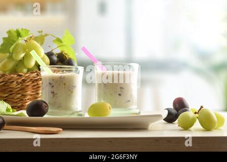 Organic grape yogurt on white plate with bunches of white and red grapes in basket on wooden table with kitchen background. Front view. Stock Photo