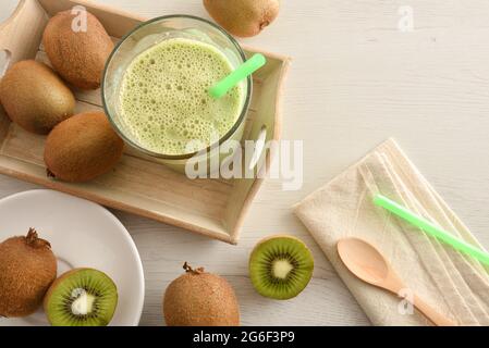 Kiwi drink in glass on wooden tray on white wooden bench full of fruits with plate napkin and spoon. Top view. Stock Photo