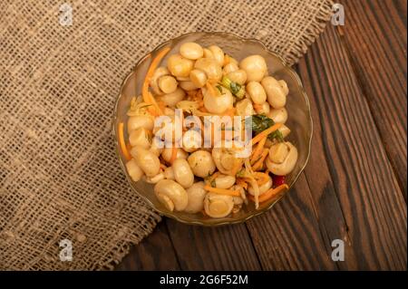 Salted mushrooms in a glass dish on a wooden table. Close-up Selective focus Stock Photo
