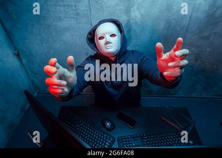 Anonymous hacker wearing face mask working on computer in dark room Stock Photo