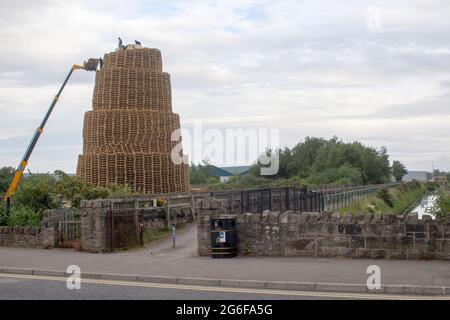 4 July 2021 Youths on top of the very tall bonfire made from thousands of wooden industrial pallets as they prepare for the 12th of July celebrations Stock Photo