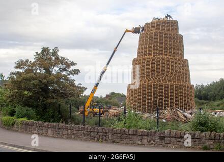 4 July 2021 Youths on top of the very tall bonfire made from thousands of wooden industrial pallets as they prepare for the 12th of July celebrations Stock Photo