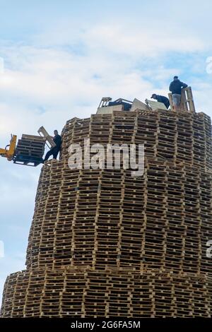 4 July 2021 Youths on top of the very tall bonfire made from thousands of wooden industrial pallets as they prepare for the 12th of July celebrations Stock Photo
