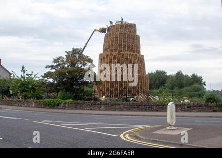 4 July 2021 Youths on top of the very tall bonfire made from thousands of wooden industrial pallets as they prepare for the 12th of July celebrations Stock Photo