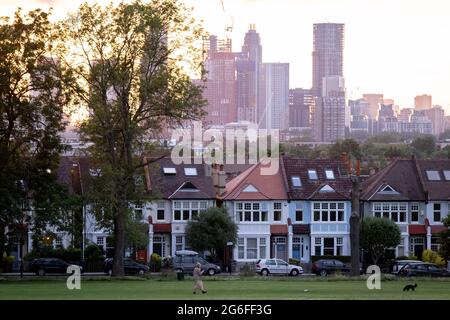 Residential high-rise towers in the distant metropolis and a setting sun behind the ash trees that form one side of Ruskin Park in Lambeth, on 4th July 2021, in London, England. Stock Photo