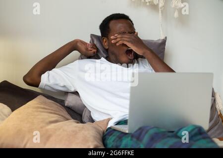 African man working lying on bed at home being tired yawning. Stock Photo