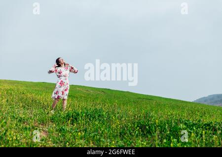 Beautiful brunette woman in a dress with flowers stands on the mountain one Stock Photo