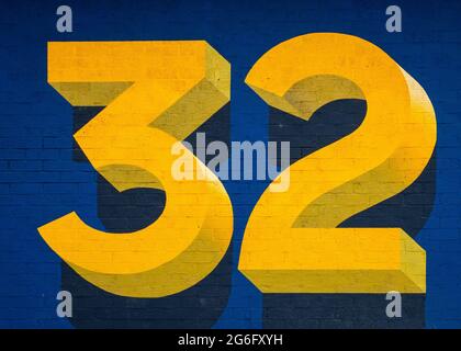 Big bright yellow three dimensional number thirty two on blue background. 32 numerals in 3d three and two. Brick texture. Stock Photo