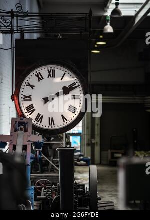 Old fashioned vintage big industry factory clock hanging with roman numerals in abandoned building no workers. Industrial workshop clocking off time Stock Photo