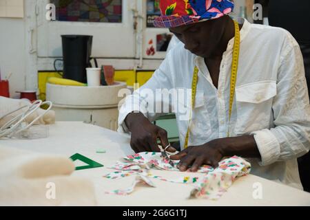 A tailor cutting fabric in his sewing shop. African man working in a workshop. Stock Photo