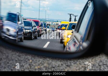 Traffic jam on European highway with big city in a background - lots of cars standing in the queue seen from the rearview mirror Stock Photo