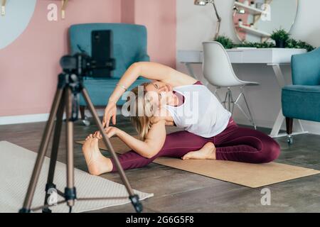 A woman in sportswear works out at home on a mat in front of a mobile phone. Online training, the use of technology for distance learning. Stock Photo