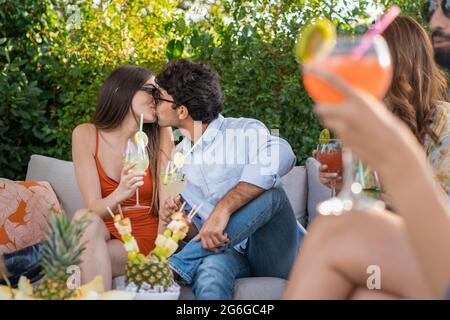 Romantic couple of young lovers kissing at terrace cocktail party. Group of people having fun gathering together. Stock Photo