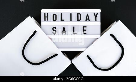 Light board with text HOLIDAY SALE with paper shopping bags. Big Sale online shopping concept. Promotion advertising. Holiday Stock Photo