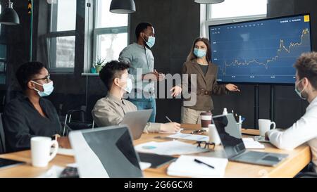 Colleagues having meeting in boardroom, woman in mask making presentation Stock Photo