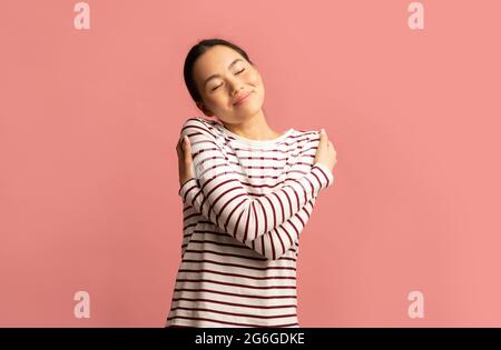 Love Yourself Concept. Pleased Young Asian Woman Embracing Herself Stock Photo