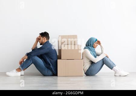 Frustrated arab couple sitting by paper boxes on floor Stock Photo