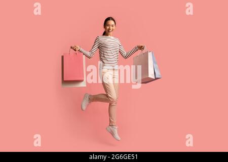Shopping Promotions. Overjoyed Young Asian Woman Jumping With Colorful Paper Shopper Bags Stock Photo