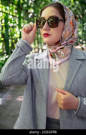 Portrait of stylish muslim lady in grey suit and sunglasses poses at park, fashion style trend. Stock Photo