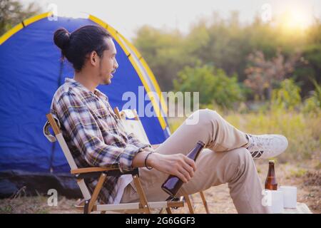 people drinking in camping, man holding bottle of beer and cheer sitting looking view near tent, freedom and happy time in vacation in sunset Stock Photo