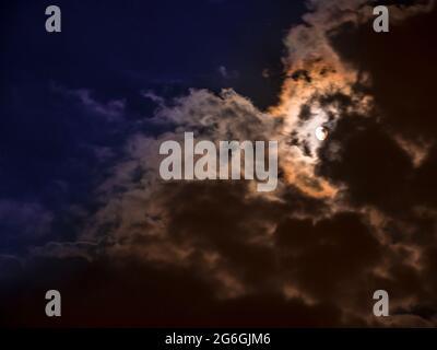 Moon covered by thick clouds in motion creates a spooky atmosphere Stock Photo
