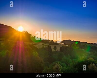 Golden sunrise over trees on the horizon of the hill with strong colorful flares and blue sky Stock Photo
