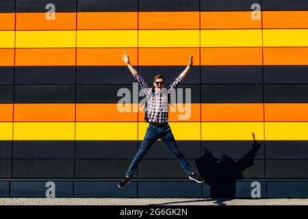 Full length, photo of funny excited young man in plaid shirt with glasses jumping high on isolated colored background, concept of victory, success, ce Stock Photo