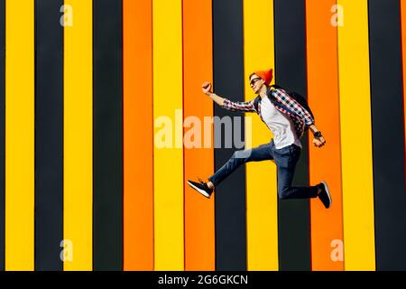 Full size photo of a cool stylish guy, wearing sunglasses and a hat, with a briefcase, jumping high, rejoicing in the winner, against the background o Stock Photo