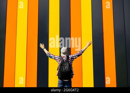 Rear view of a happy young man, with a briefcase, with his hands up, an excited man with his hands up, on against a colorful colorful wall Stock Photo