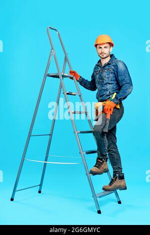 Full length portrait of handsome male construction worker climbing on ladder over blue background looking to camera Stock Photo