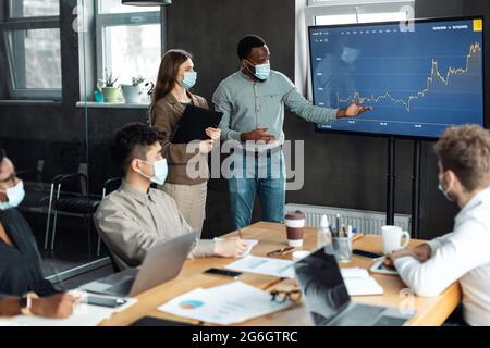 Colleagues having meeting in boardroom, man in mask making presentation Stock Photo