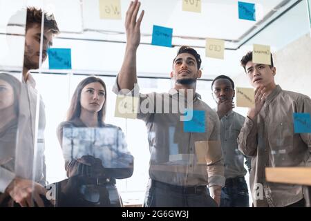 Diverse colleagues brainstorming using sticky notes on glass wall Stock Photo
