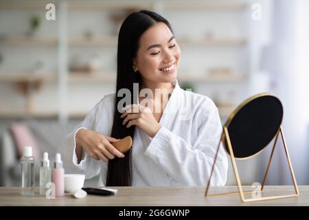 Cheerful asian lady combing hair with wooden brush Stock Photo