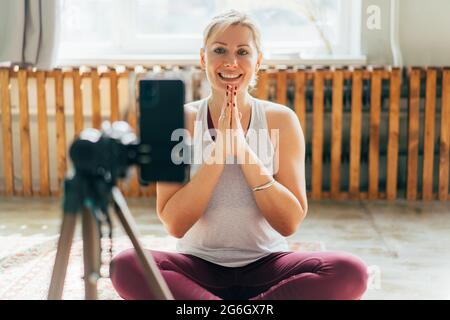 A modern yoga instructor welcomes the community to a lesson in online streaming and records the lesson on a phone camera. Online classroom teaching. Stock Photo