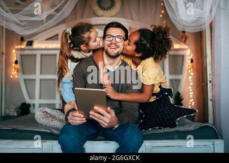 Multiethnic children and father having fun, playing on tablet at home Stock Photo