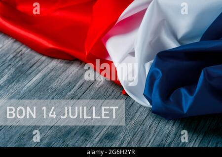 the text bon 14 juillet, happy 14 july, the national day of france written in french, and a french flag on a gray rustic wooden background Stock Photo