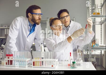 Young scientists look at a test tube with a red substance in the laboratory. Stock Photo