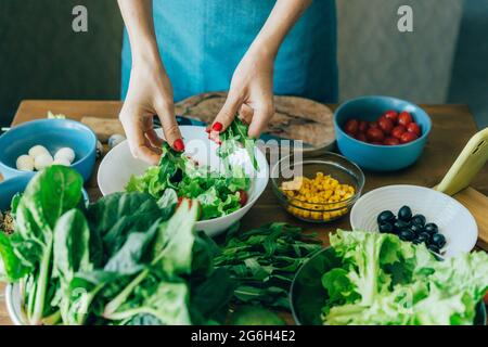 Top view of the kitchen table with ingredients for preparing a salad of European cuisine and the female hands of the cook. Stock Photo