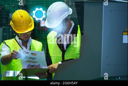 Asian engineers male female in Industrial wear hard hats in Industry manufacturing factory mechanical display interface arm robot manufacturing indust Stock Photo